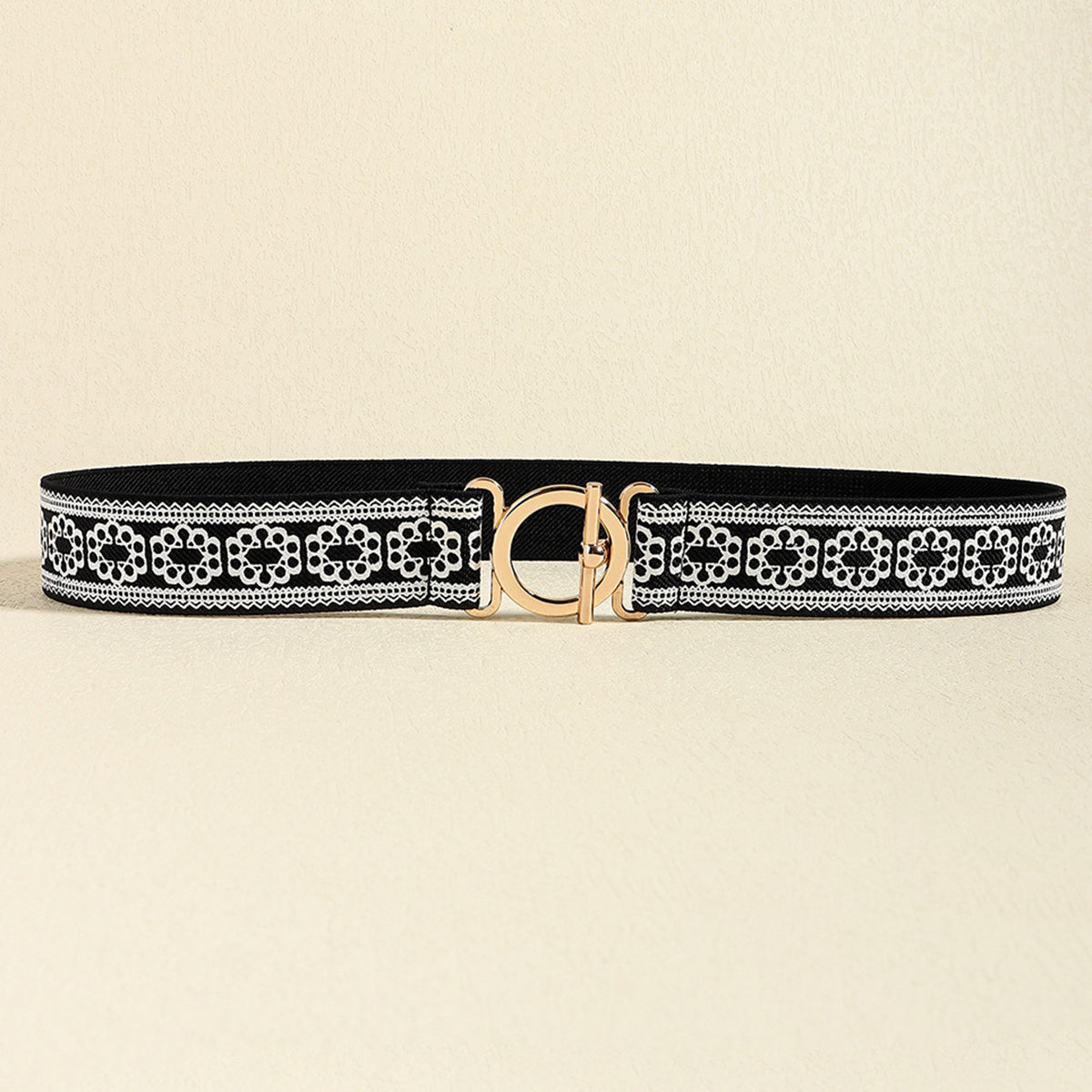 Black elastic belt with a white ornamental pattern and polished gold-tone toggle clasp, featuring a slim profile and flexible construction.