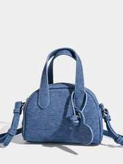 A mini blue canvas crossbody bag with twin top handles, a rounded structured silhouette, and an adjustable shoulder strap with metal attachments.