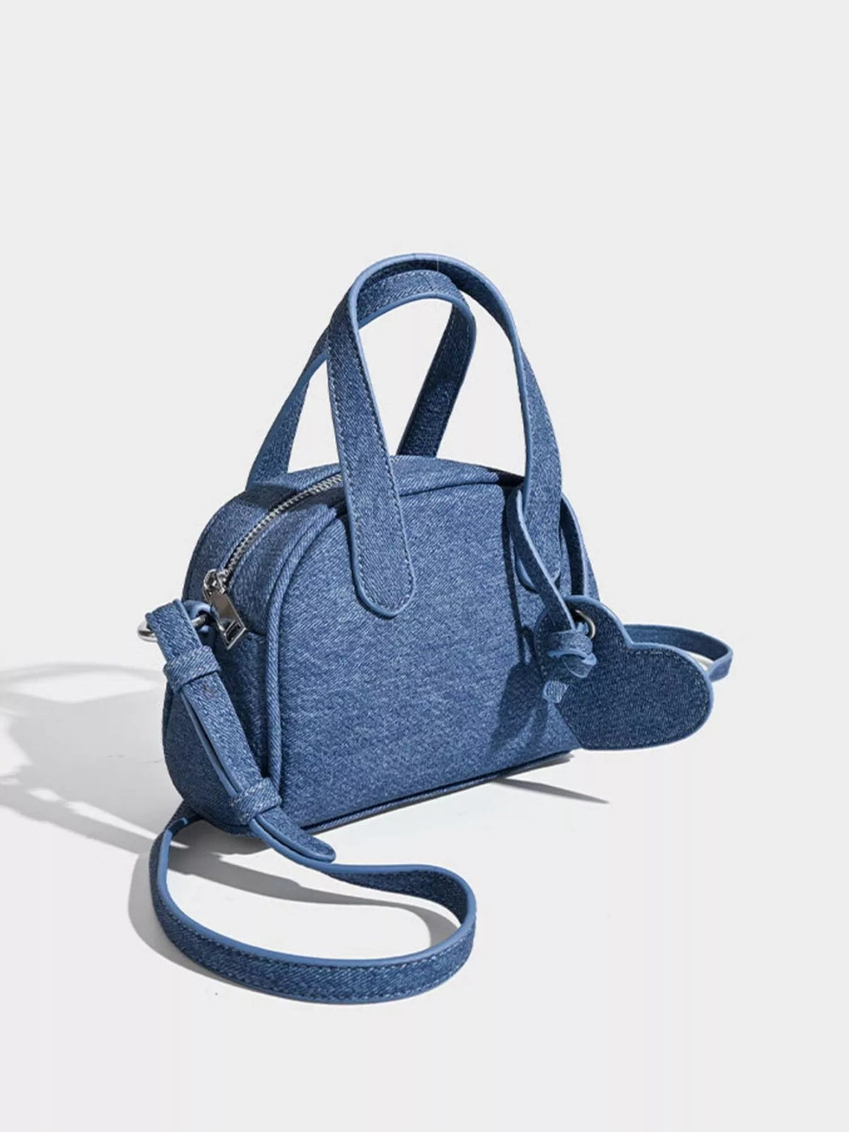 A mini blue canvas top-handle crossbody bag features dual handles, a zippered top, and a long adjustable strap.