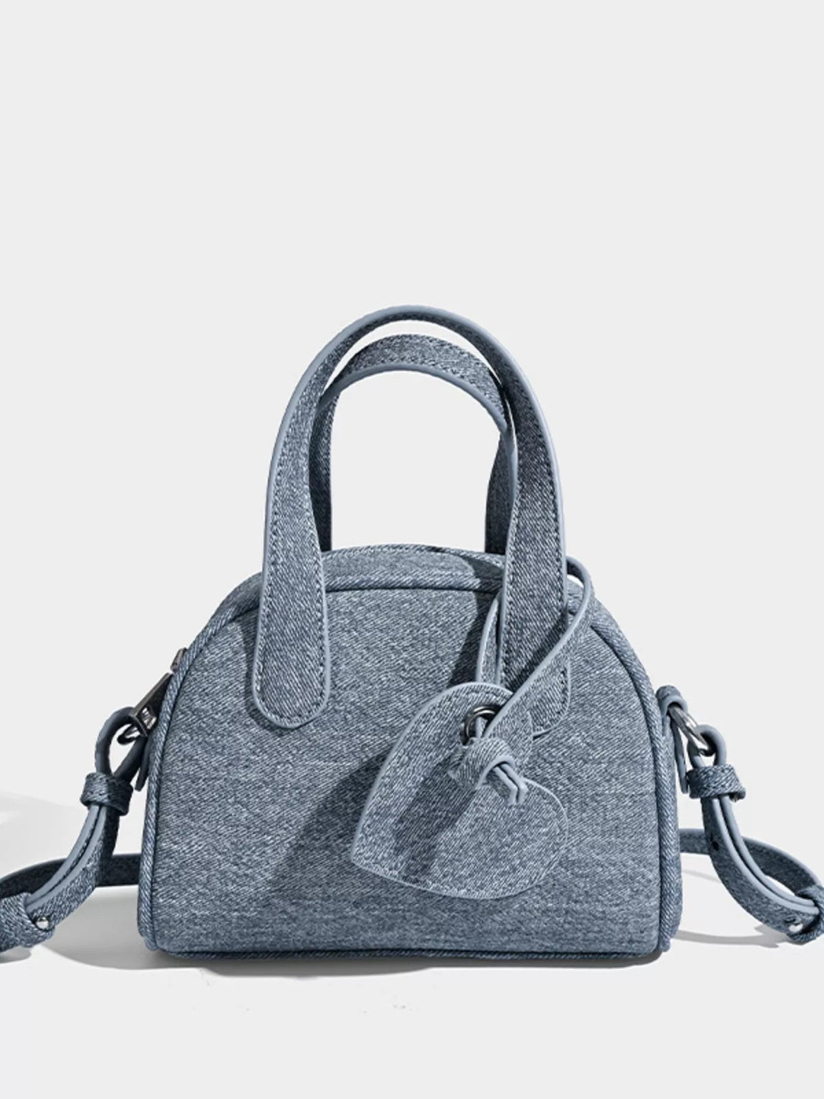 Mini gray canvas crossbody bag with dual top handles, adjustable shoulder strap, rounded structured silhouette, and a front flap pocket.