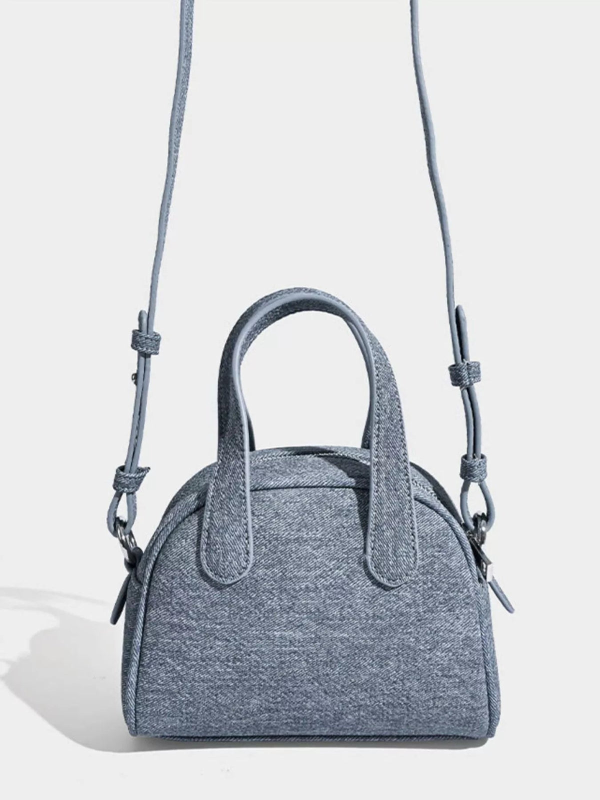 Gray mini canvas crossbody bag with a structured rounded silhouette, dual top handles, adjustable shoulder strap, and visible side hardware.