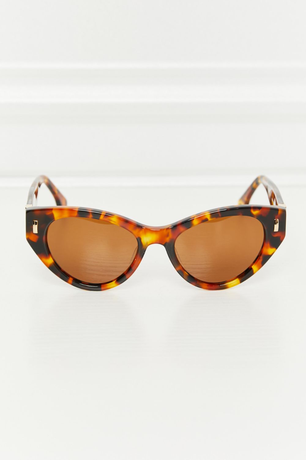 Tangerine tortoiseshell acetate cat-eye sunglasses feature a sculpted upswept silhouette, warm brown lenses, and polished metal temple accents.