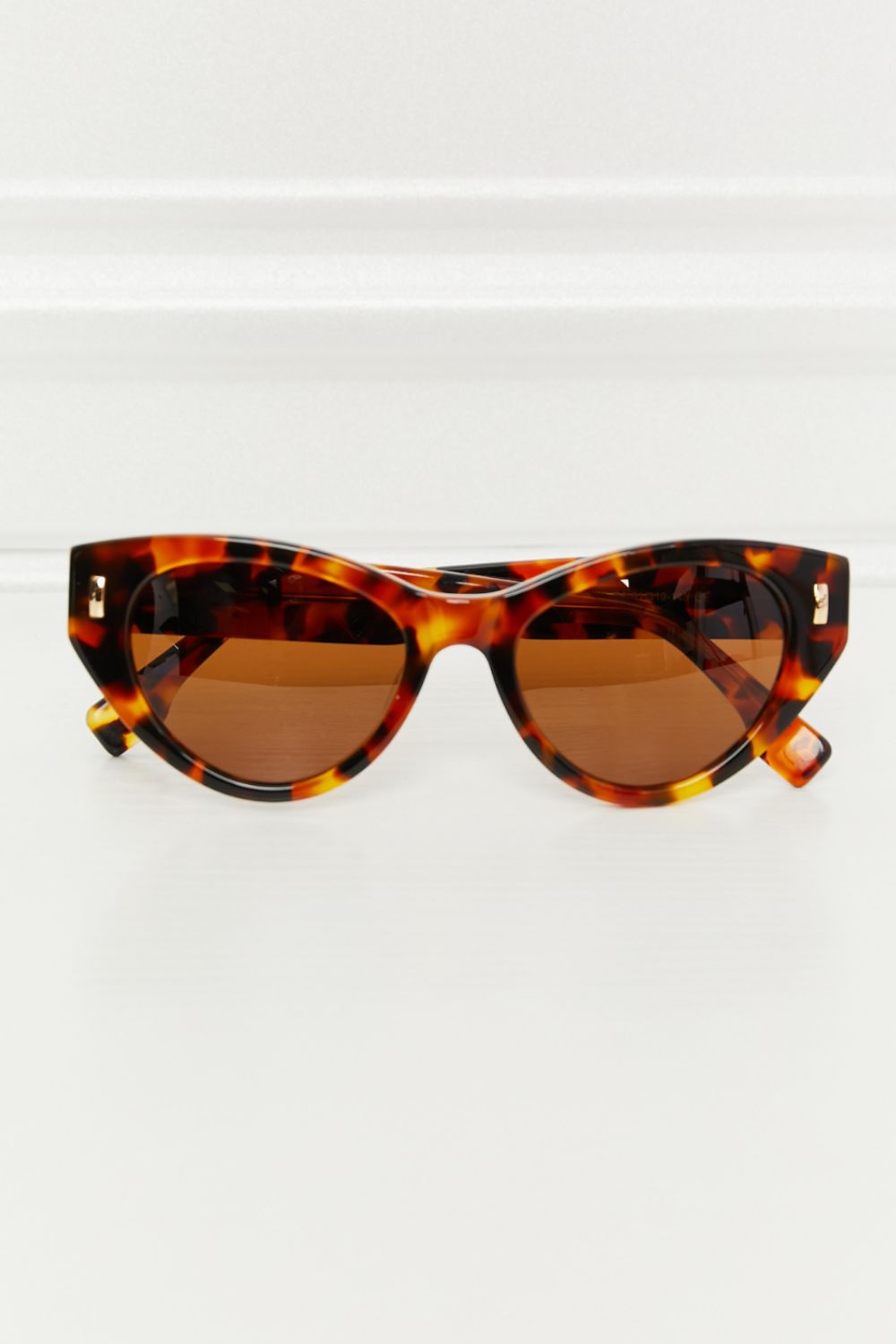 Tangerine tortoiseshell acetate cat-eye sunglasses feature a bold sculpted frame, upswept corners, dark brown lenses, and polished metal accents.