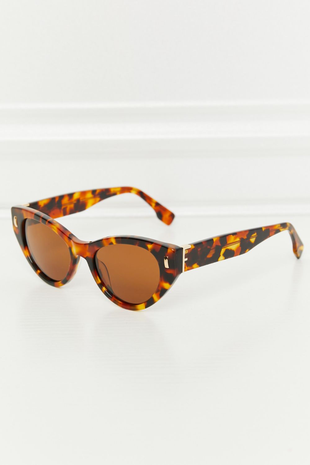 Tangerine tortoiseshell acetate cat-eye sunglasses feature a sculpted upswept silhouette, mottled frame, matching temples, and warm brown lenses.