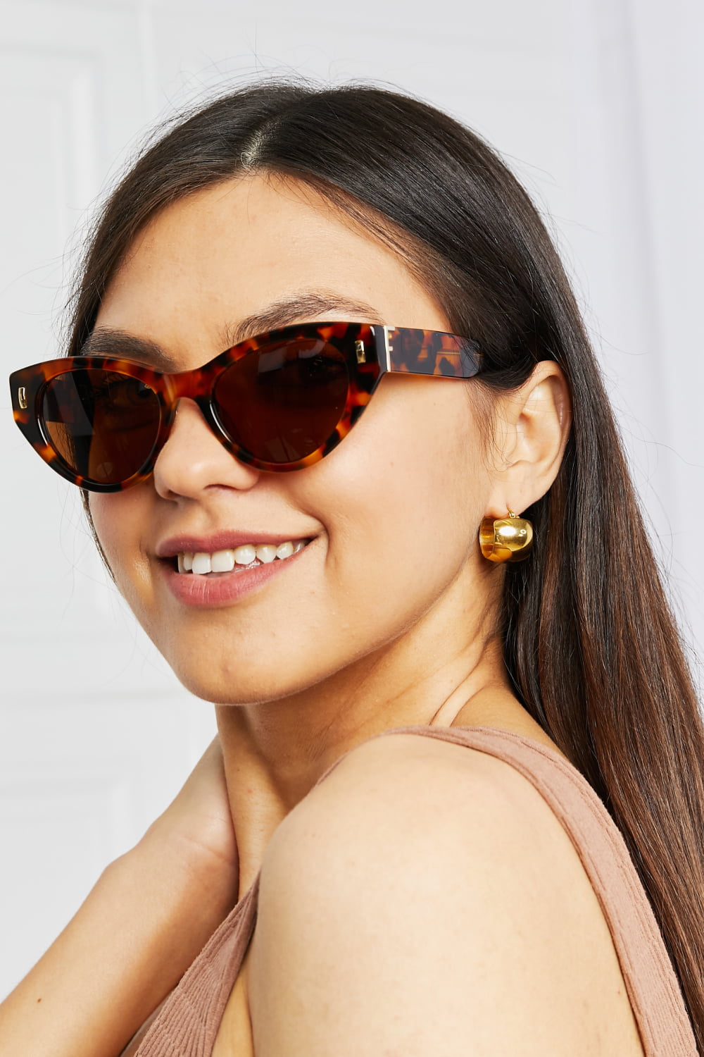 Model smiling in a three-quarter pose wears tangerine tortoiseshell acetate cat-eye sunglasses with sculpted upswept frames and dark polarized lenses.