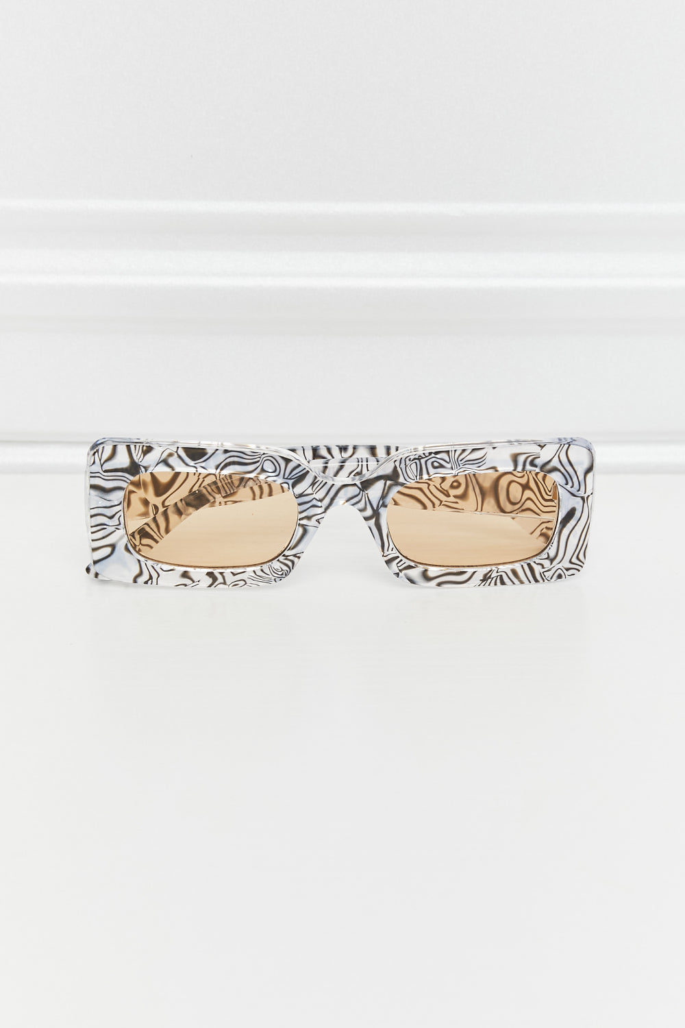 Patterned rectangle polycarbonate sunglasses feature a bold structured frame with warm tinted lenses and thick temples for a polished statement look.