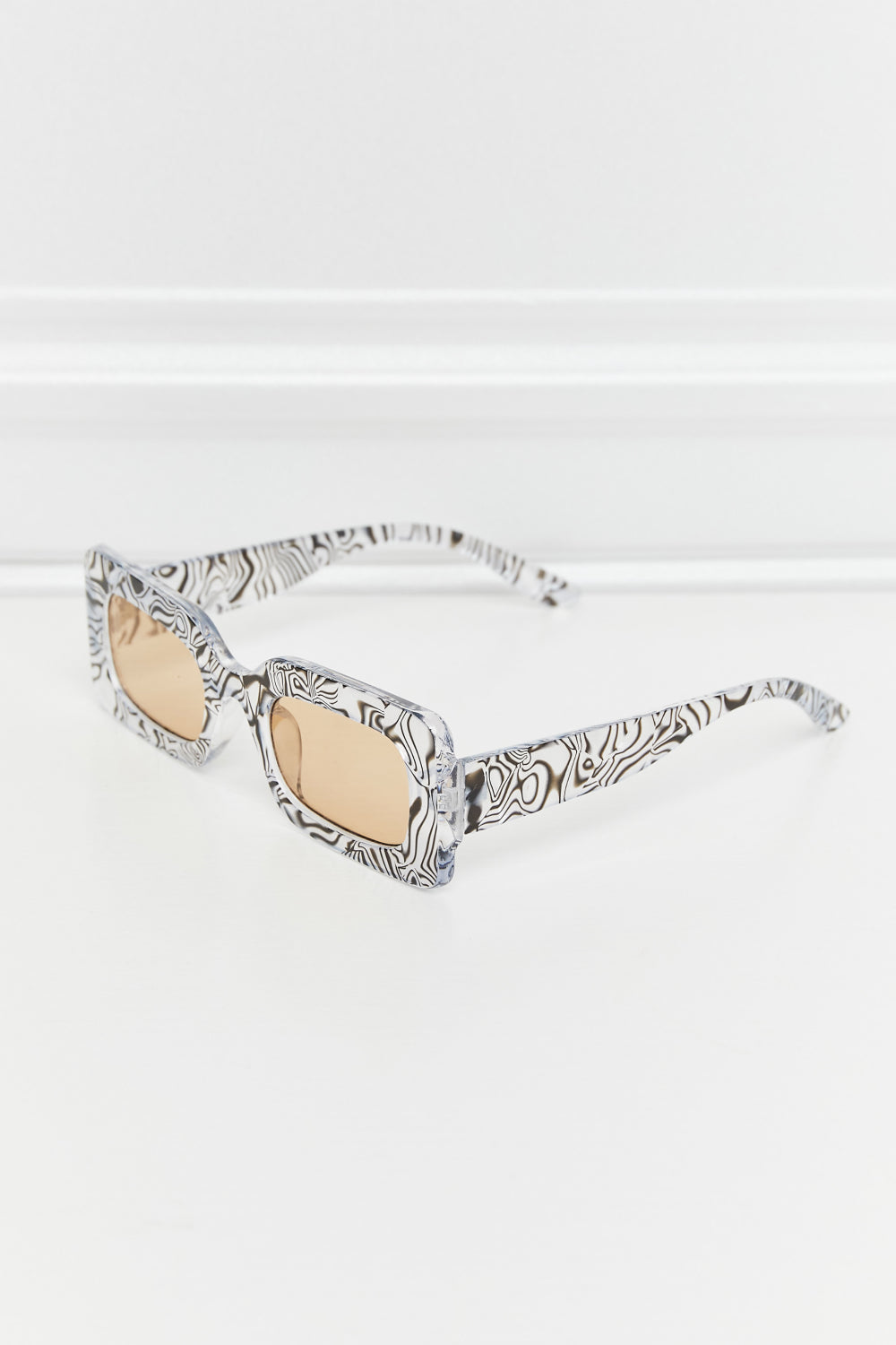 Rectangle polycarbonate sunglasses with a bold black-and-white patterned frame, brown-tinted lenses, and open temples shown at an angled view.