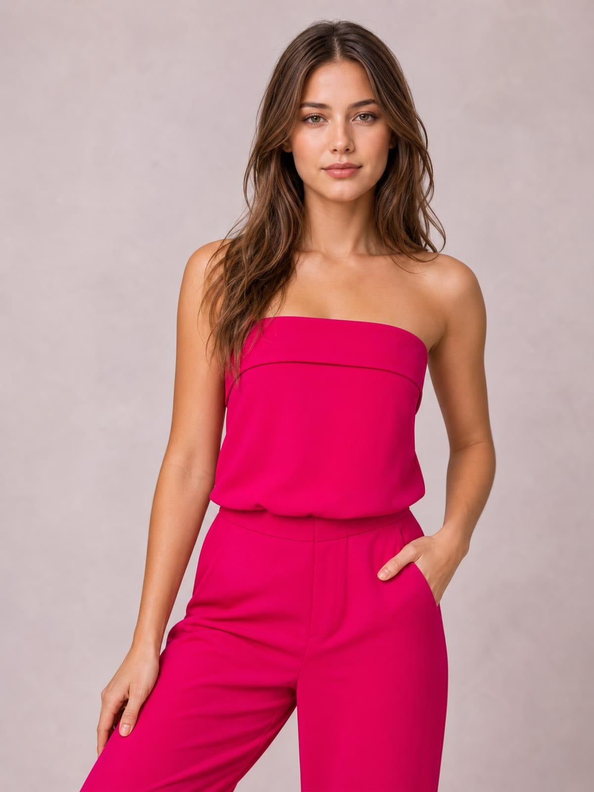 Model poses with one hand in the pocket of a hot pink strapless tube top and wide-leg pants set, featuring a clean silhouette and tailored construction.