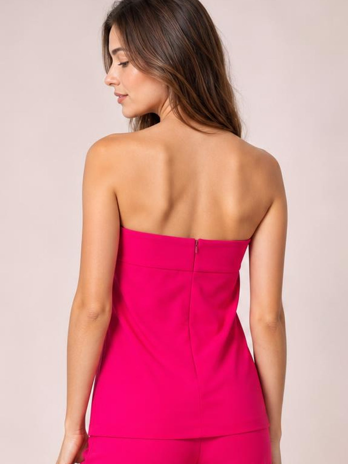 Model turned away to show the back of a hot pink strapless tube top with a structured fit, straight hem, and center-back zipper.