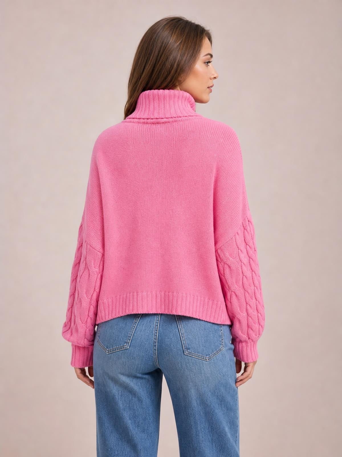 Model shown from behind wearing a bright pink solid cable-knit turtleneck sweater with long sleeves, ribbed cuffs and hem, and a relaxed regular-length silhouette.