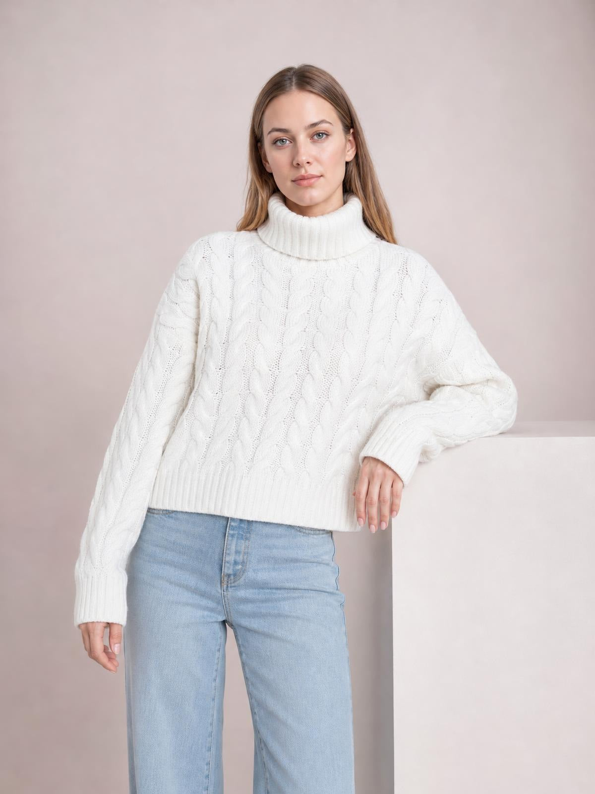 Model wears a white cable-knit turtleneck sweater with long sleeves, a relaxed regular silhouette, and ribbed collar, cuffs, and hem.
