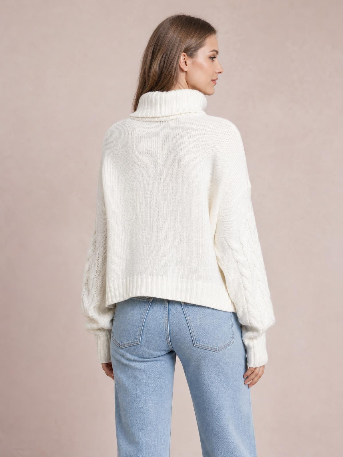 A model poses in a rear three-quarter view wearing an ivory solid turtleneck sweater with long cable-knit sleeves, ribbed cuffs, and a regular-length silhouette.