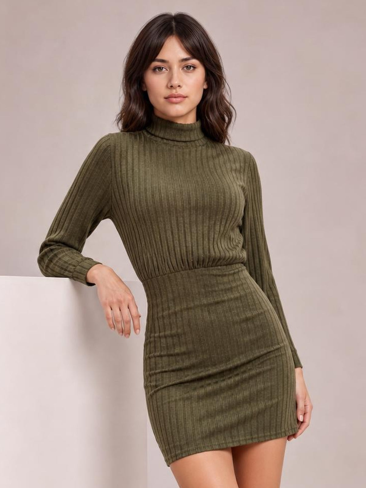 A model leans with one hand resting on a surface, wearing an olive green turtleneck bodycon ribbed knit dress with long sleeves and a mini-length silhouette.