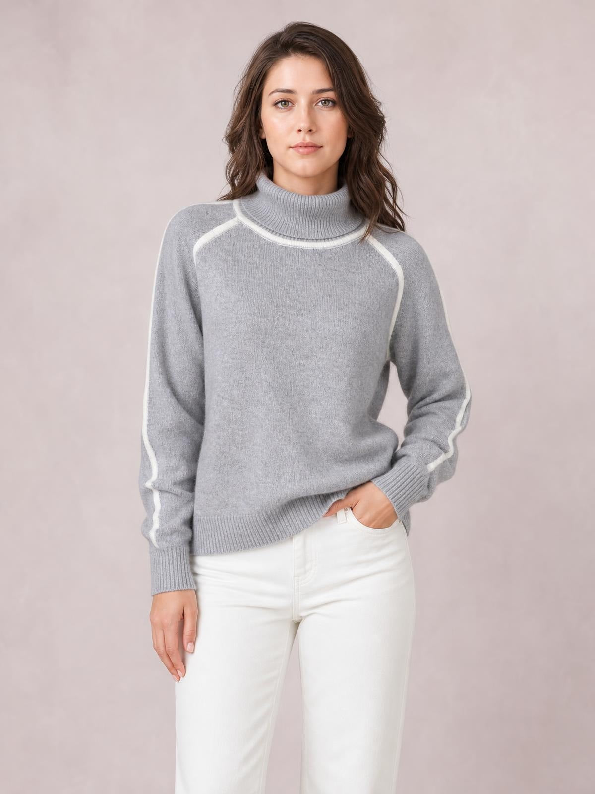 Woman wearing a gray turtleneck contrast trim sweater with ribbed collar, cuffs, and hem, relaxed silhouette, and one hand in her pocket.