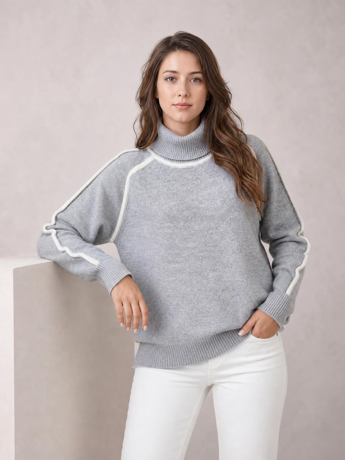 Model wearing a light gray turtleneck sweater with contrast white trim, ribbed collar, cuffs, and hem, relaxed silhouette, posing with one hand in a pocket.