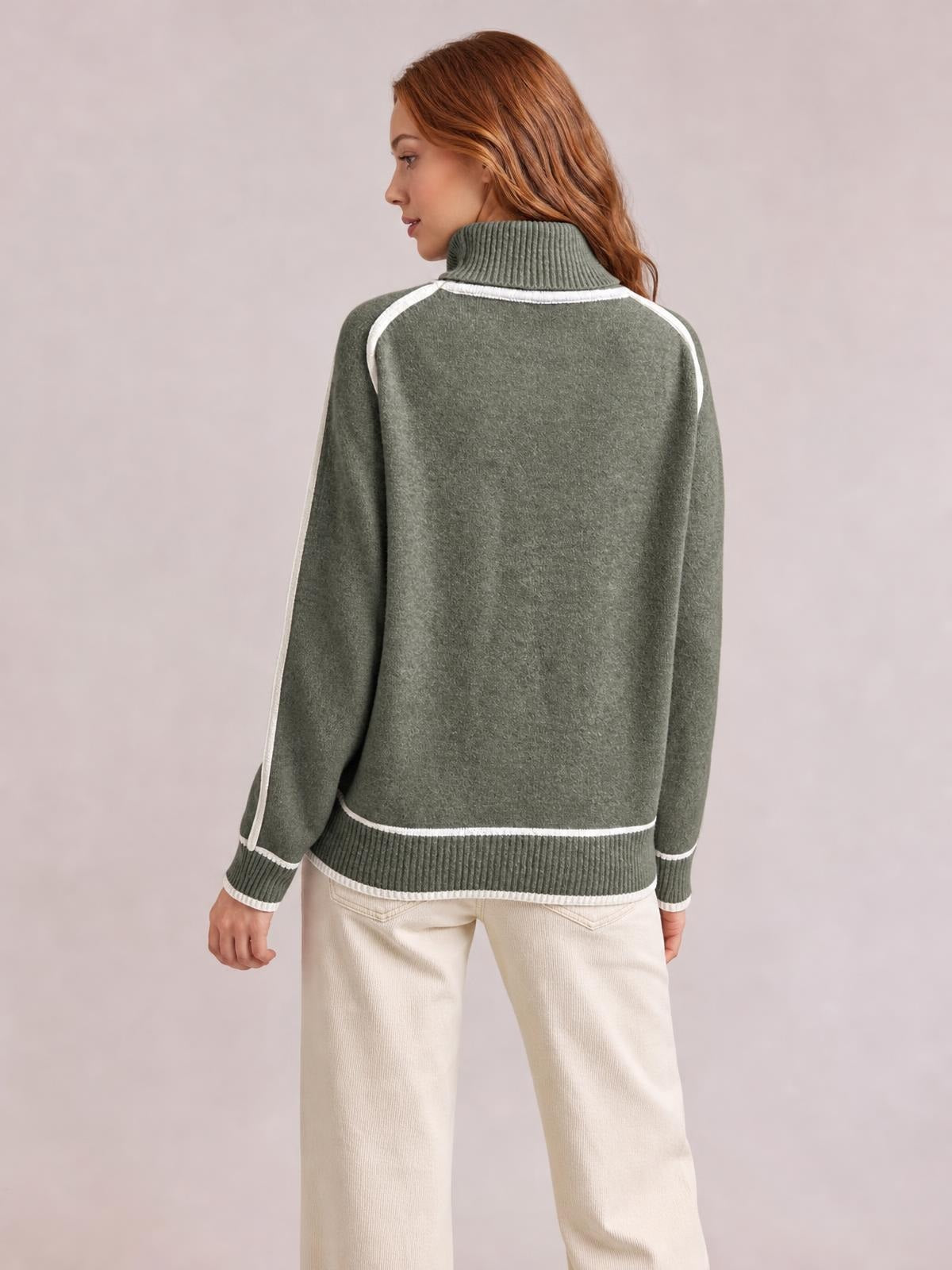 Model shown from the back in a relaxed stance wearing a sage green turtleneck sweater with contrast white trim, ribbed cuffs and hem.