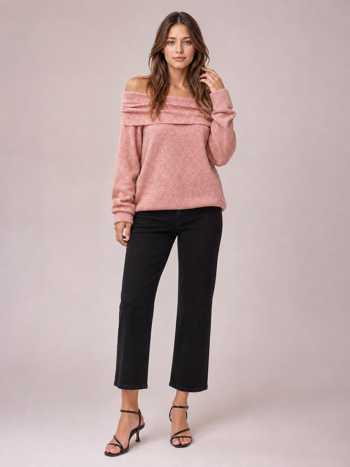 Model wears a soft pink long-sleeve sweater with an off-shoulder neckline, relaxed silhouette, ribbed cuffs and hem, posing with one hand in her hair.