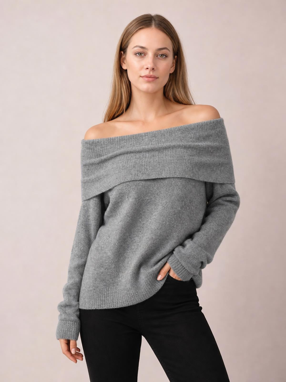 Model wears a gray long-sleeve sweater with a wide folded off-shoulder neckline, relaxed silhouette, ribbed cuffs and hem, posing with one hand in a pocket.