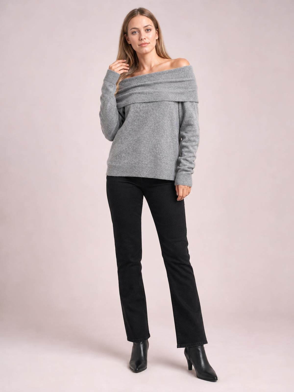 Model wearing a gray long-sleeve sweater with a wide folded off-shoulder neckline, ribbed cuffs and hem, relaxed silhouette, and one hand touching her hair.