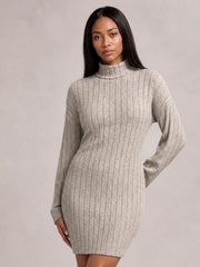 Model poses in a light taupe turtleneck ribbed knit dress with long sleeves, vertical ribbing, a fitted silhouette, and a straight above-knee hem.