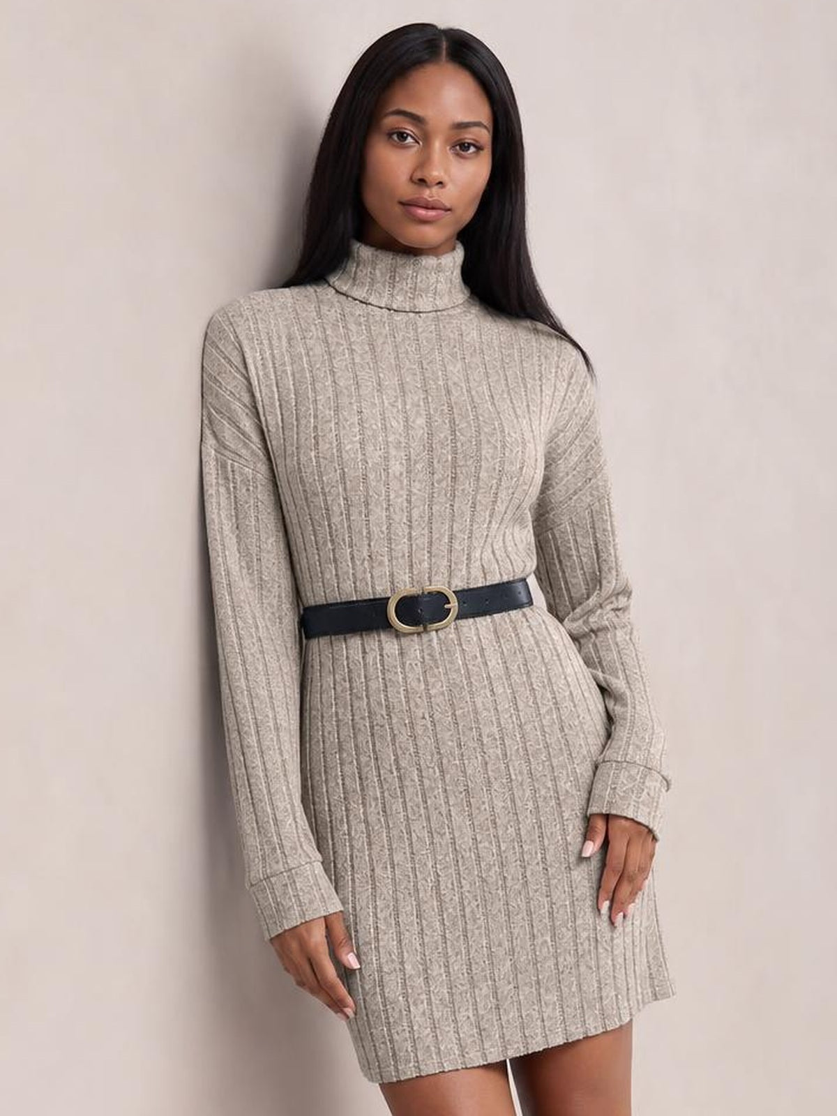Model wearing a taupe turtleneck ribbed knit dress with long sleeves, vertical texture, a straight mini silhouette, and a black waist belt.