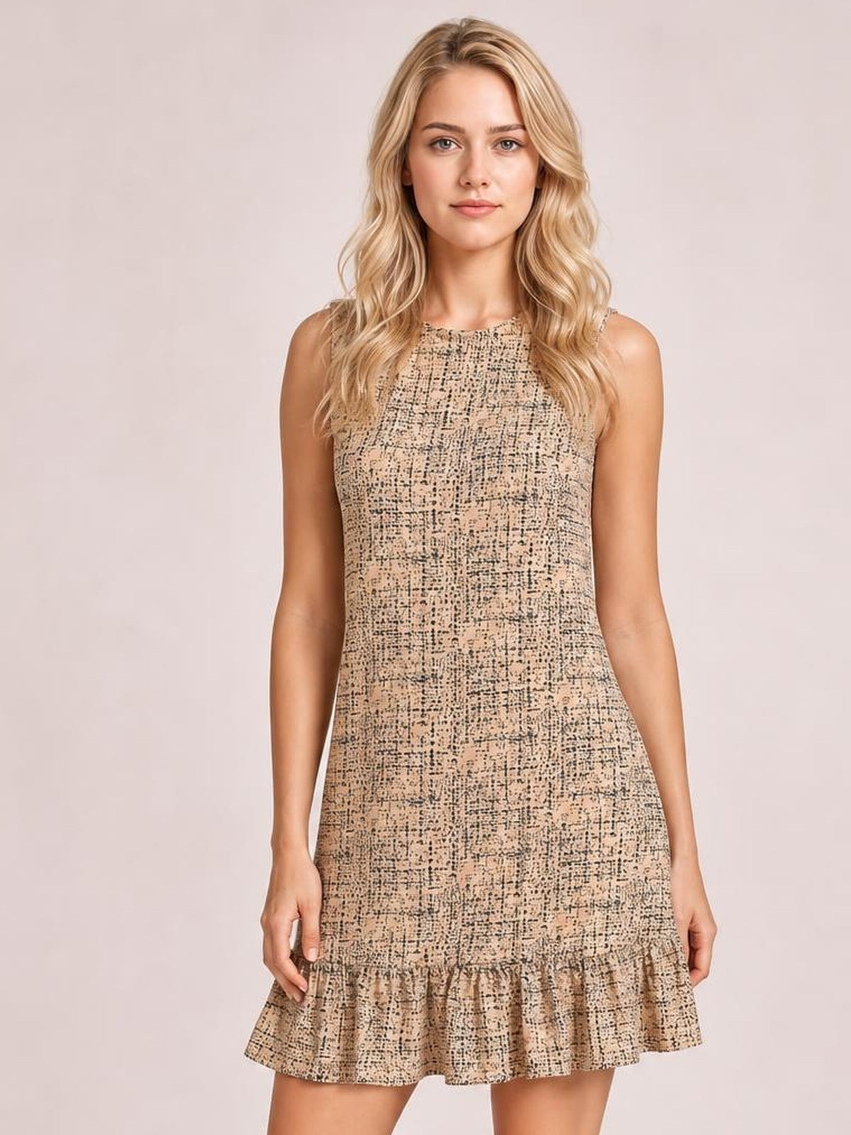 Model stands facing forward in a beige tweed sleeveless mini dress with a fitted silhouette, round neckline, and flared ruffle hem.