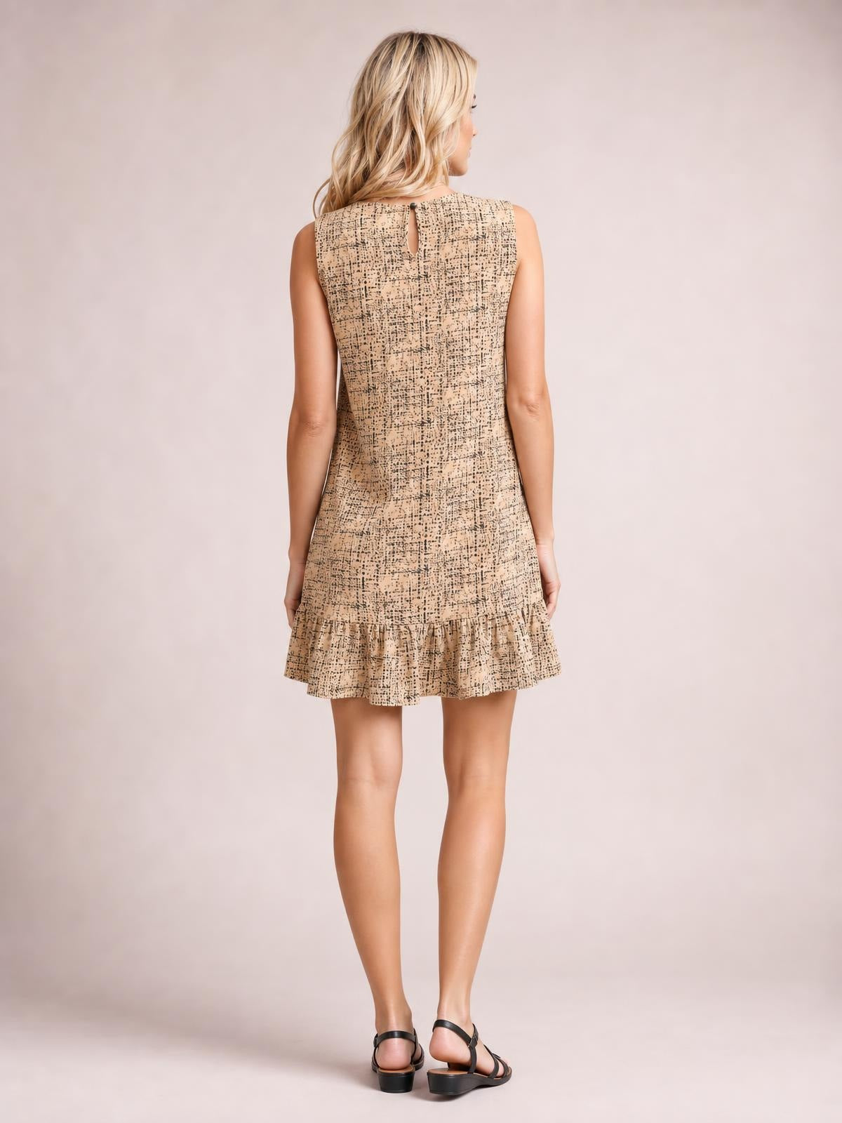 Model viewed from behind wearing a beige tweed sleeveless mini dress with a fitted silhouette, back keyhole closure, and gathered ruffle hem.