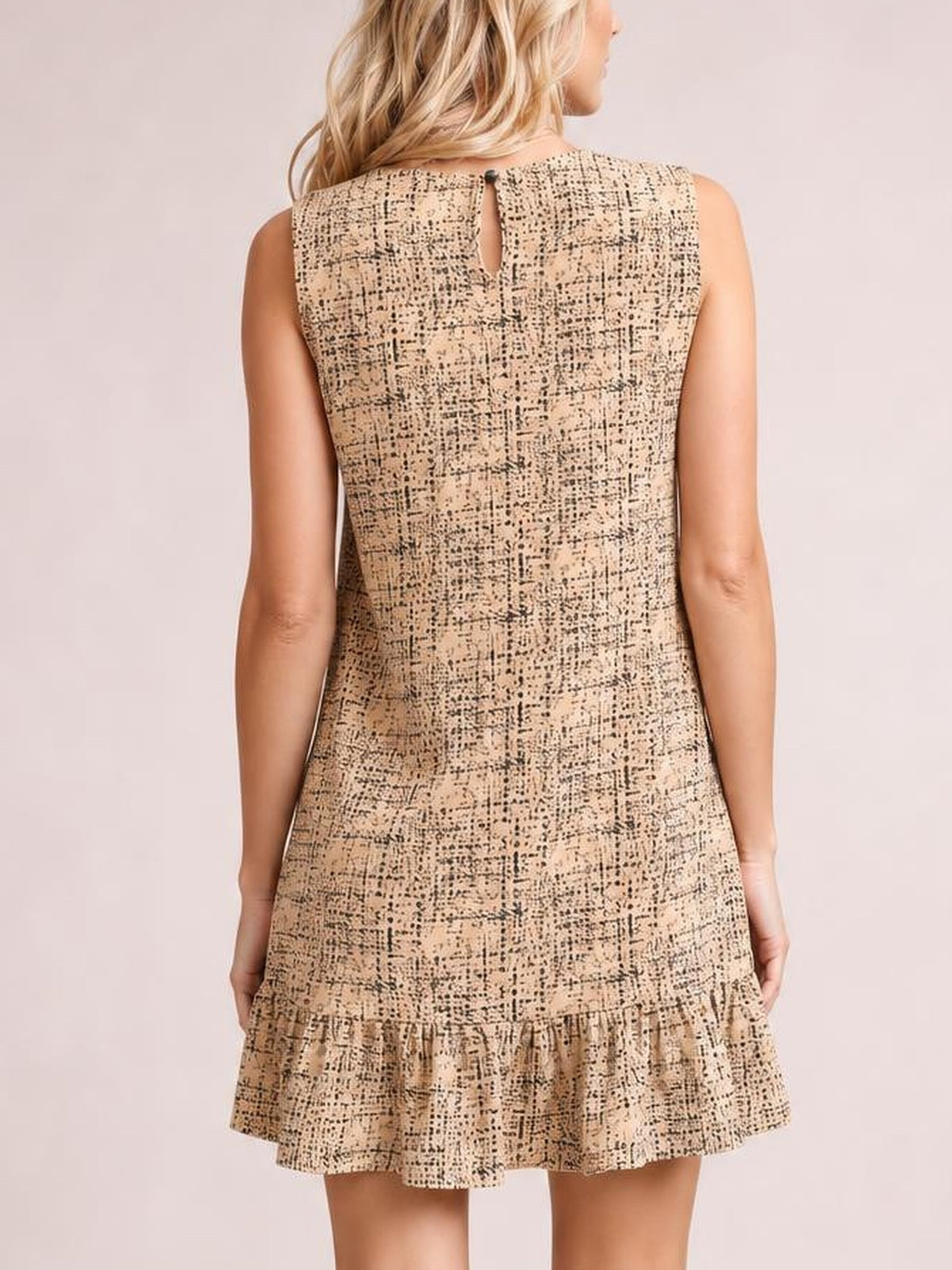 Model viewed from the back wearing a beige tweed sleeveless mini dress with a straight silhouette, back keyhole closure, and ruffle hem.