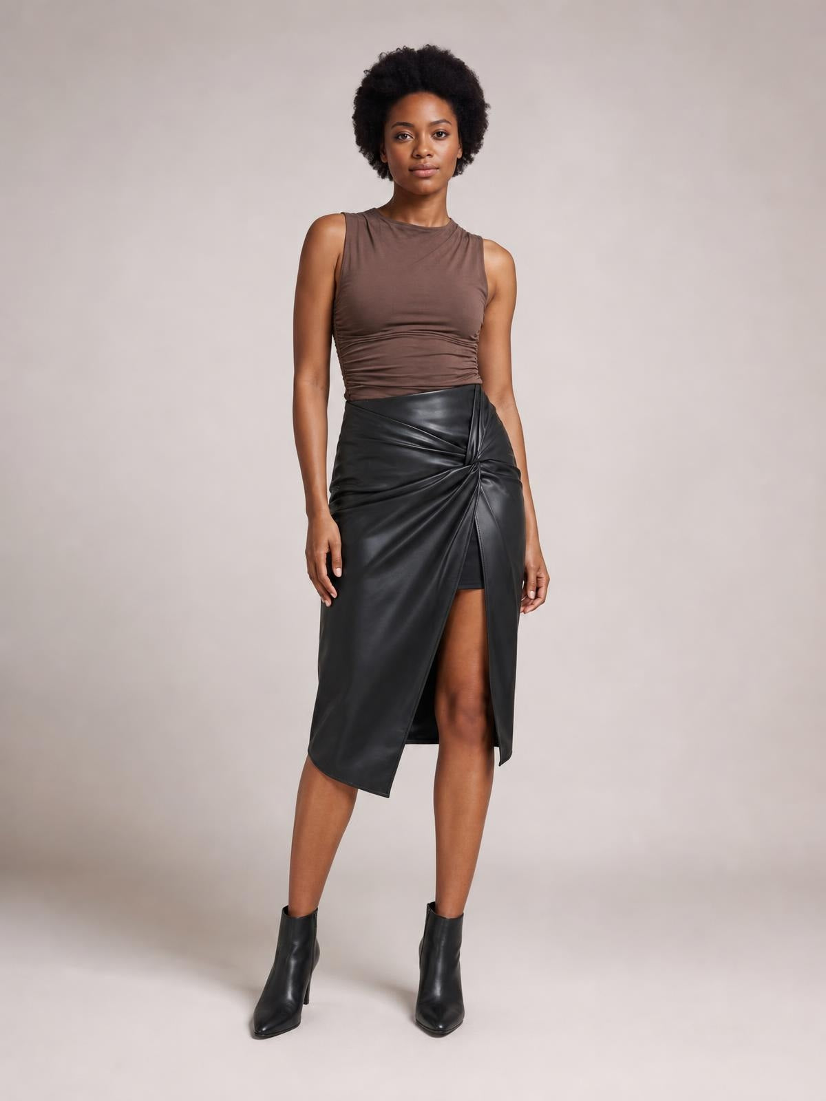Model stands in a relaxed pose wearing a black high-waist skirt with twisted front detail, draped construction, and a stylish thigh-high slit.