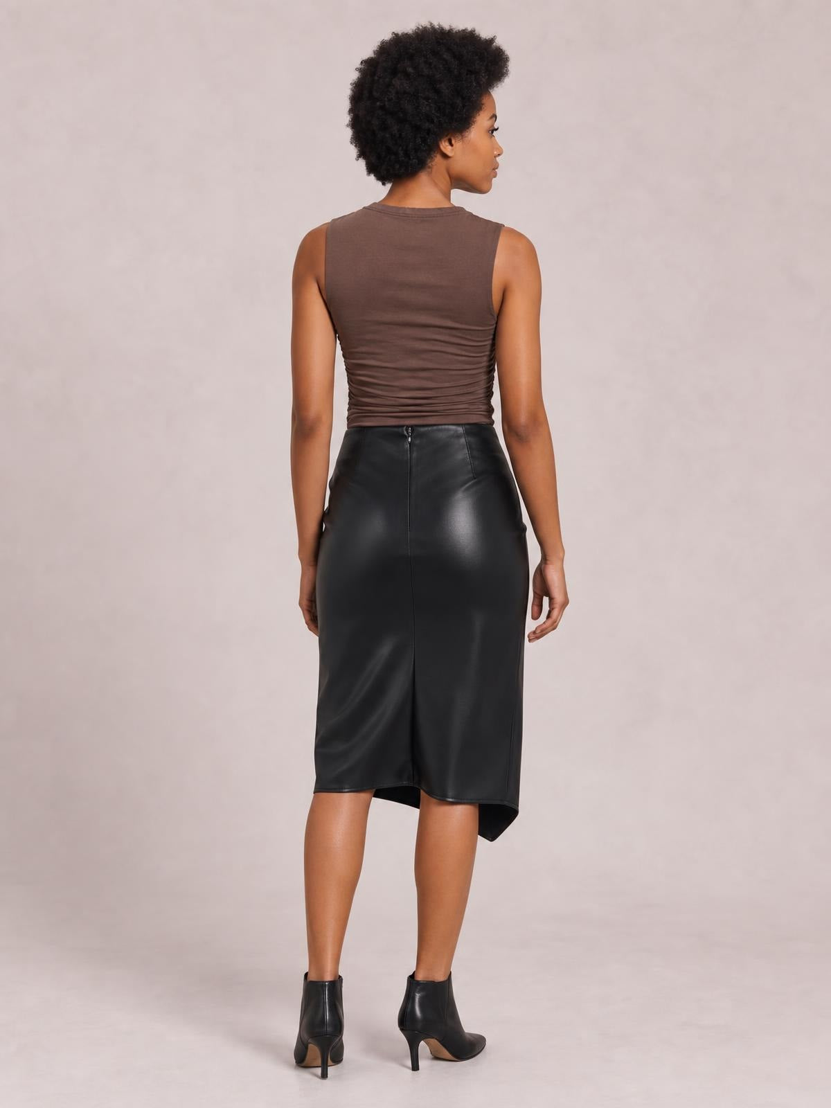 A model poses from the back wearing a black high-waist midi skirt with a fitted silhouette, center-back seam, and slit at the hem.