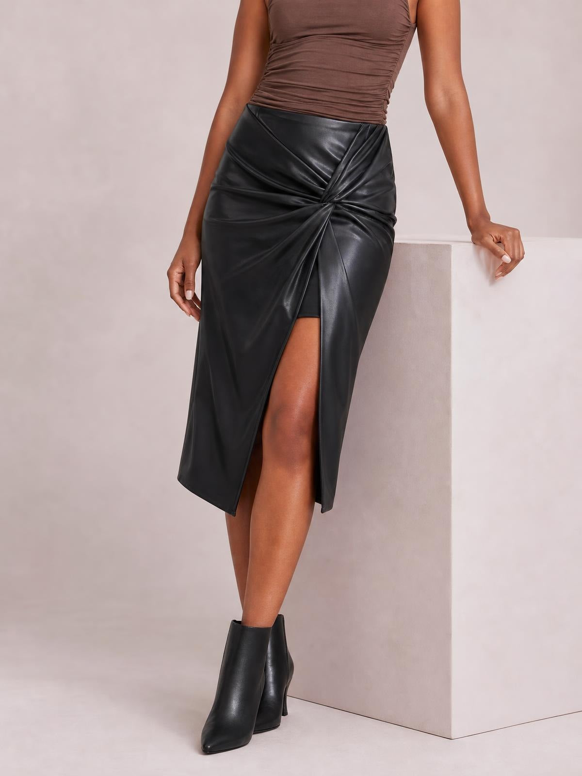 Model wears a black high-waist midi skirt with a twisted front detail, gathered construction, and a dramatic thigh-high slit.
