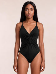 Model stands facing forward in a black twisted crisscross V-neck one-piece swimsuit with thin straps, ruched center detailing, and a high-cut silhouette.