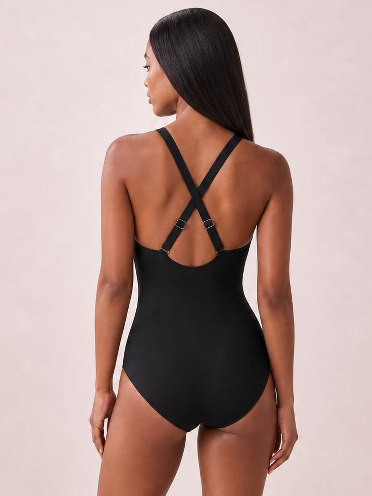Model shown from the back in a black one-piece swimsuit with crisscross adjustable straps, an open back, and a smooth, high-cut silhouette.
