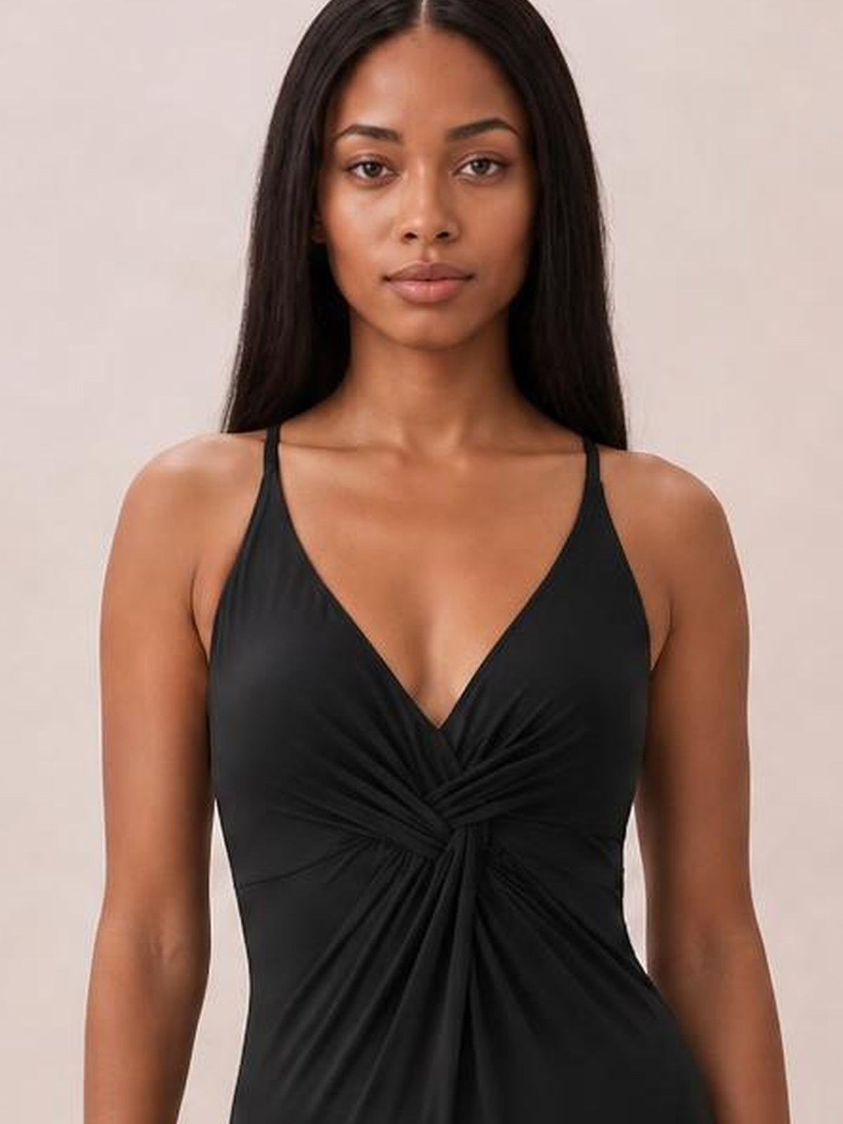 Model wearing a black twisted crisscross V-neck one-piece swimsuit with thin straps and ruched detailing gathered at the center front.
