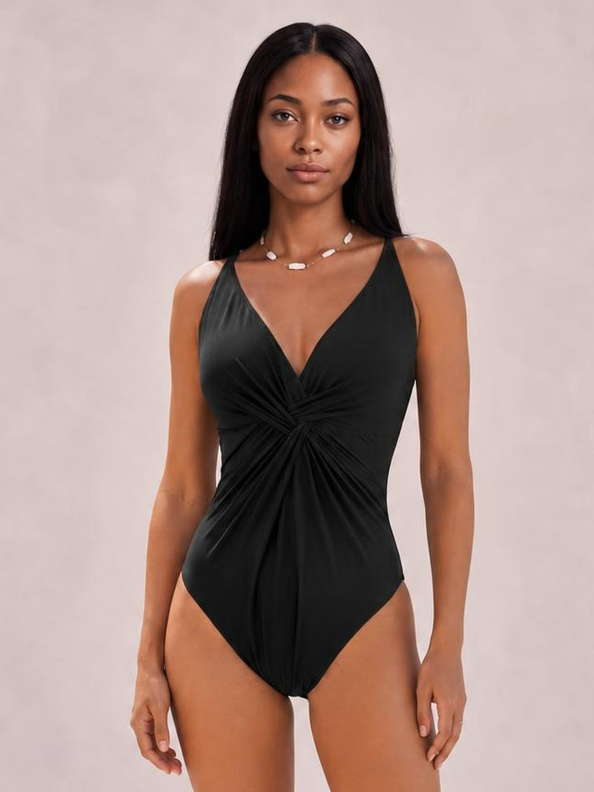 Model wears a black twisted crisscross V-neck one-piece swimsuit with ruched front detailing, slim straps, and a sleek fitted silhouette.