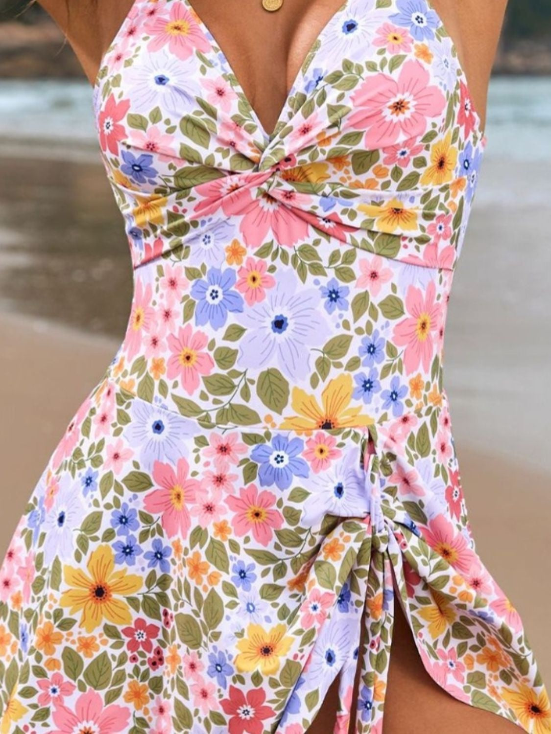 Model wears a floral-print one-piece swimsuit with a twisted front, crisscross bodice detail, thin straps, and a stretchy, fitted silhouette.