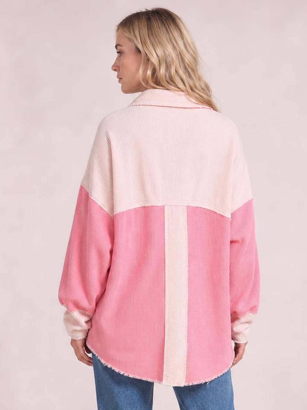 Model shown from behind wearing an oversized two-tone pink and cream corduroy shacket with exposed seams, long sleeves, and a raw hem.