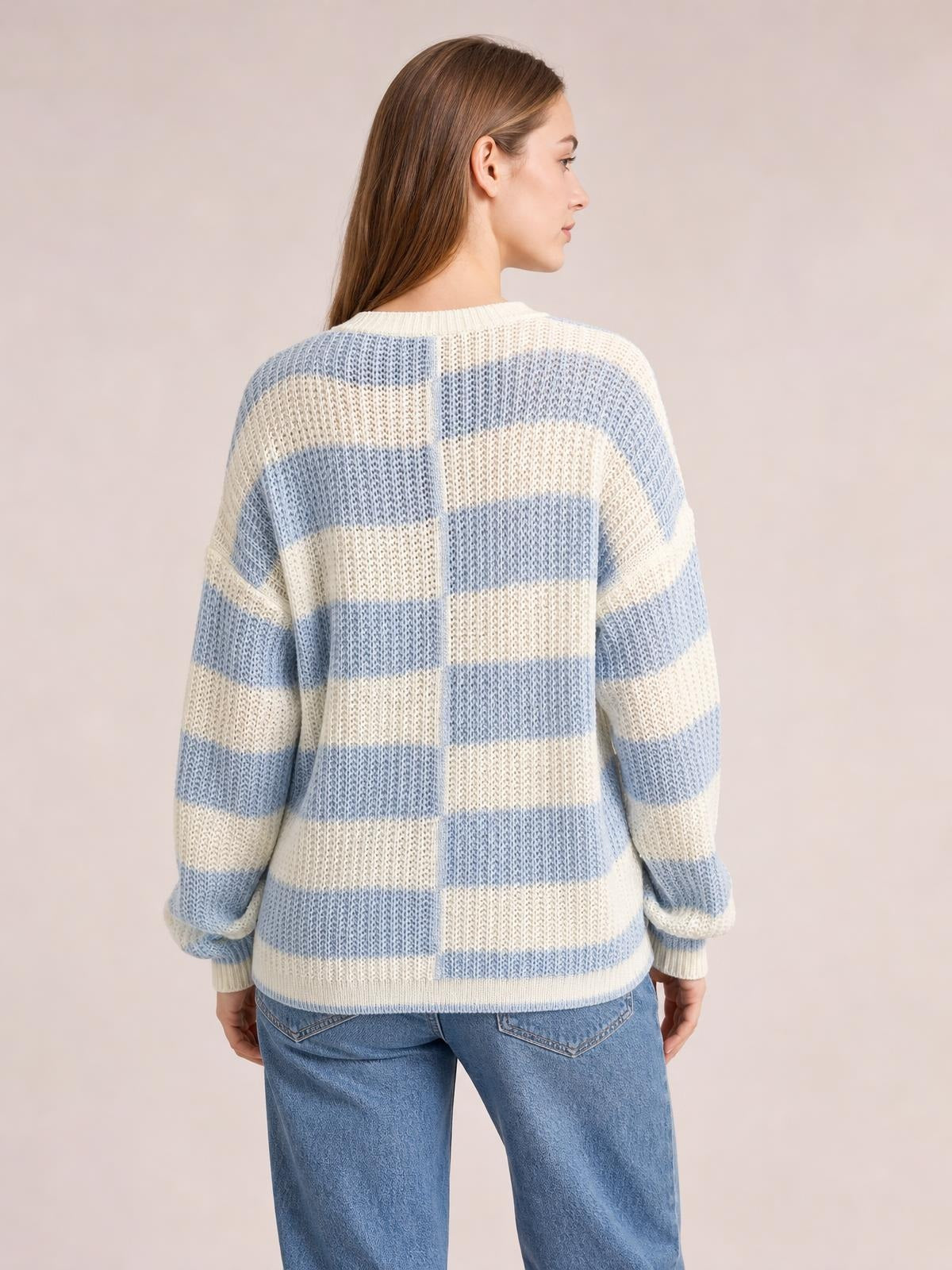 A model turned away wears a relaxed two-tone dropped shoulder sweater in blue and cream with a crew neck, color-blocked stripes, ribbed cuffs, and hem.