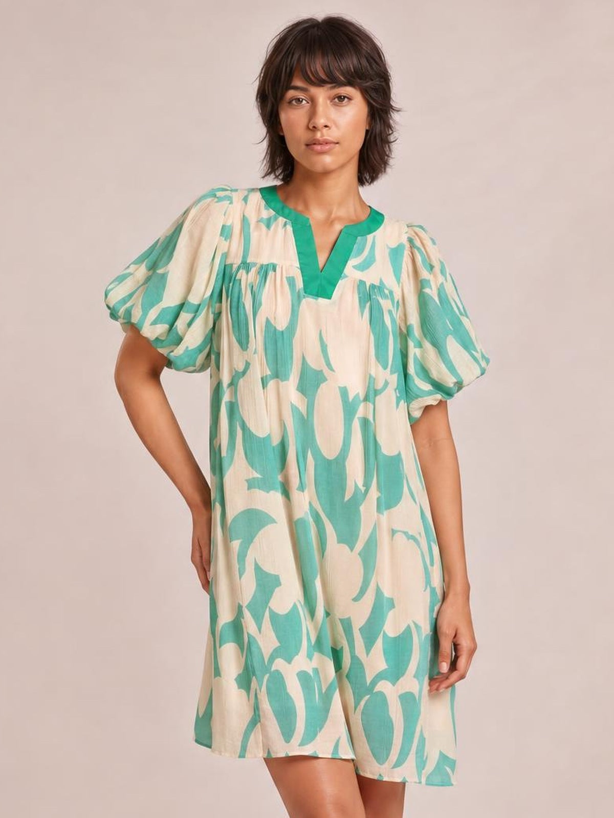 Model poses in a mint green and beige abstract print shift dress with a V-neckline, puff sleeves, relaxed silhouette, and short hem.