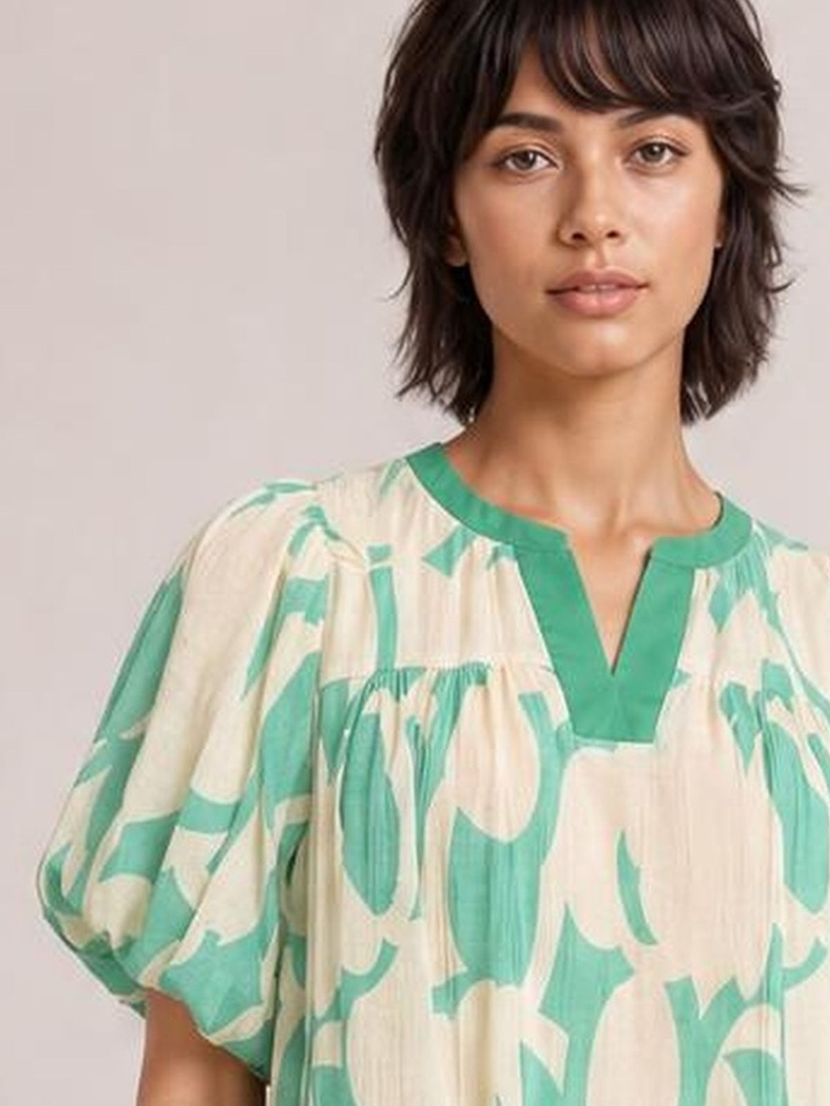 A model faces forward in a mint green and beige abstract print shift dress with puff sleeves, a V-neckline, and a relaxed, flowy silhouette.