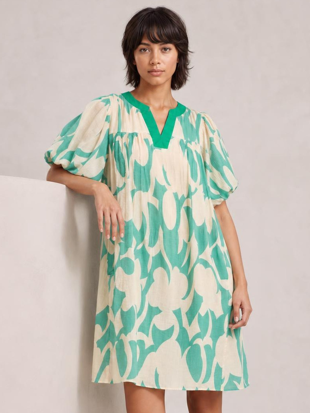 A model wears a mint green and beige abstract-print shift dress with a V-neckline, puff short sleeves, and a relaxed mini silhouette.