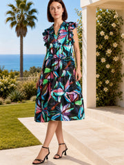 Model poses in a flowing dark leaf print midi dress with colorful botanical accents, double-layered ruffle sleeves, and a tiered A-line skirt.