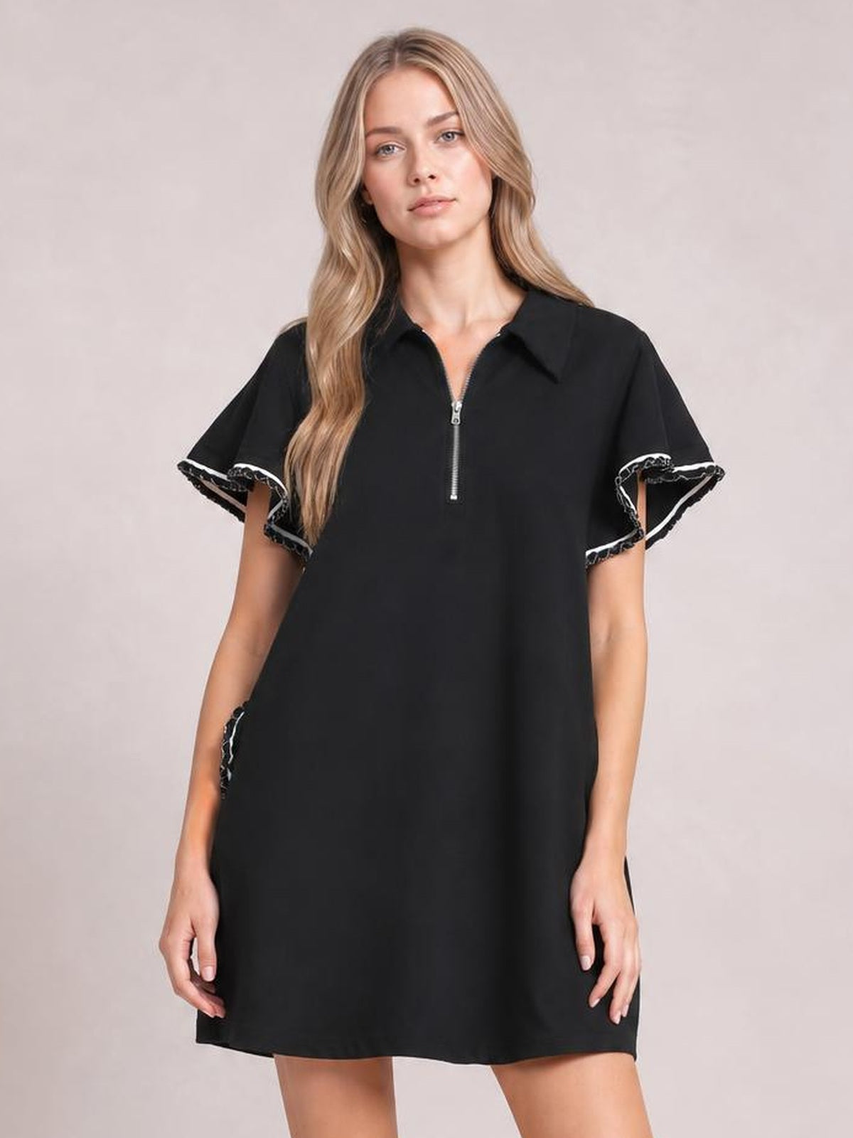 A model stands in a black mini dress with a half-zip front, ruffled butterfly sleeves, relaxed straight silhouette, contrast stitching, and side pockets.