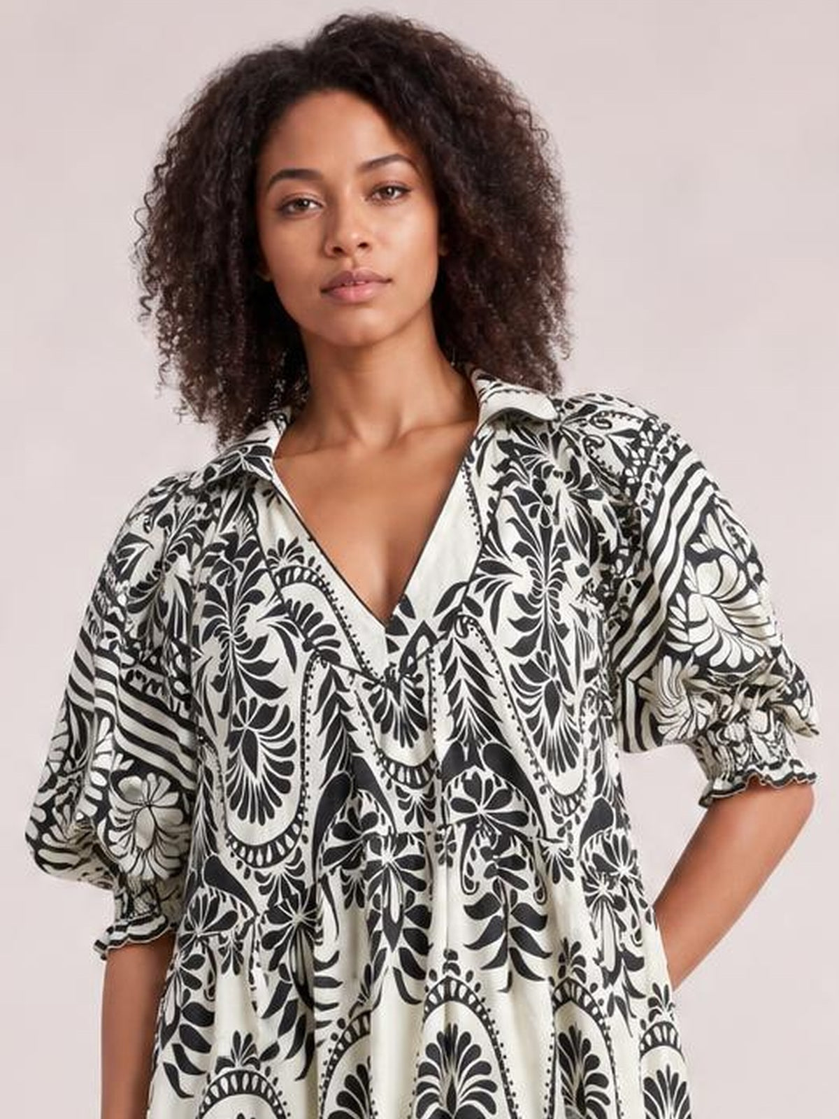 Model poses with one hand in a pocket wearing a black-and-white two-tone border print midi dress with a V-neck, three-quarter sleeves, and a flowy tiered silhouette.