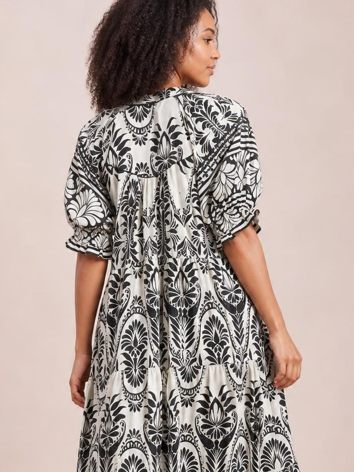 Model shown from the back wearing a black-and-white two-tone border print midi dress with puff sleeves, tiered construction, and a flowy relaxed silhouette.