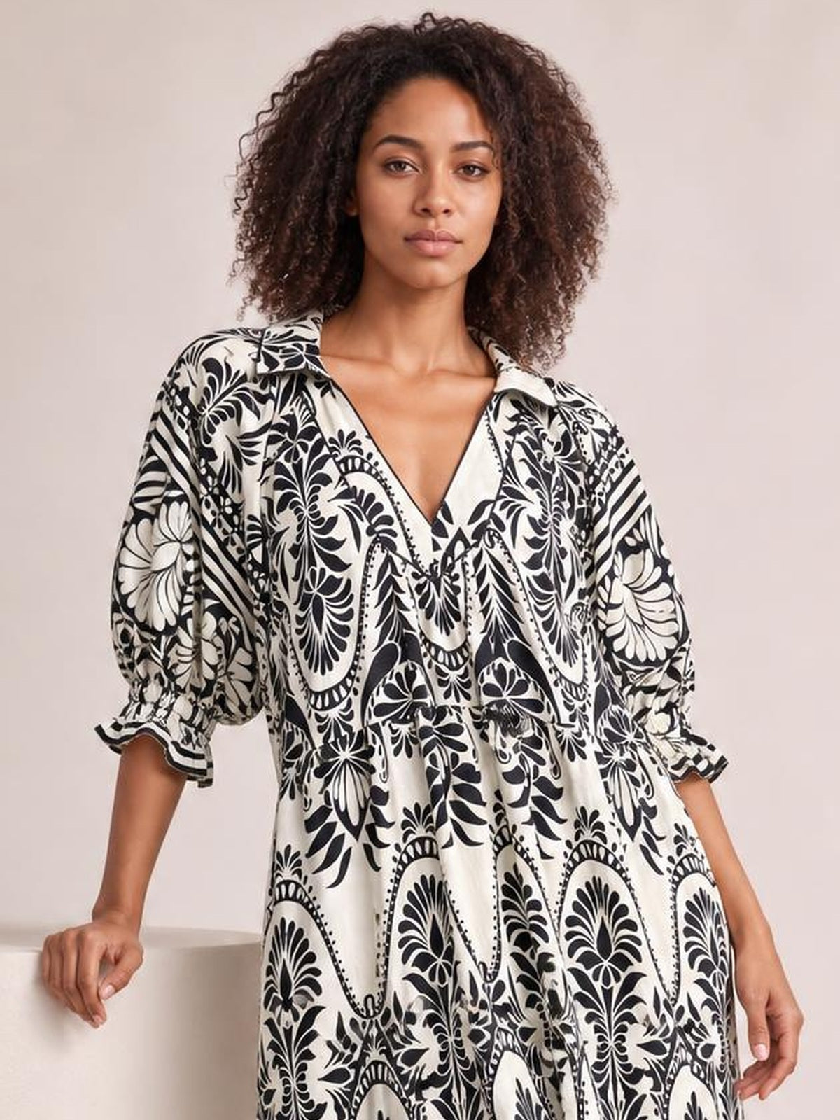 A model poses in a flowy black-and-white two-tone border print midi dress with a V-neckline, tiered silhouette, and voluminous three-quarter sleeves.