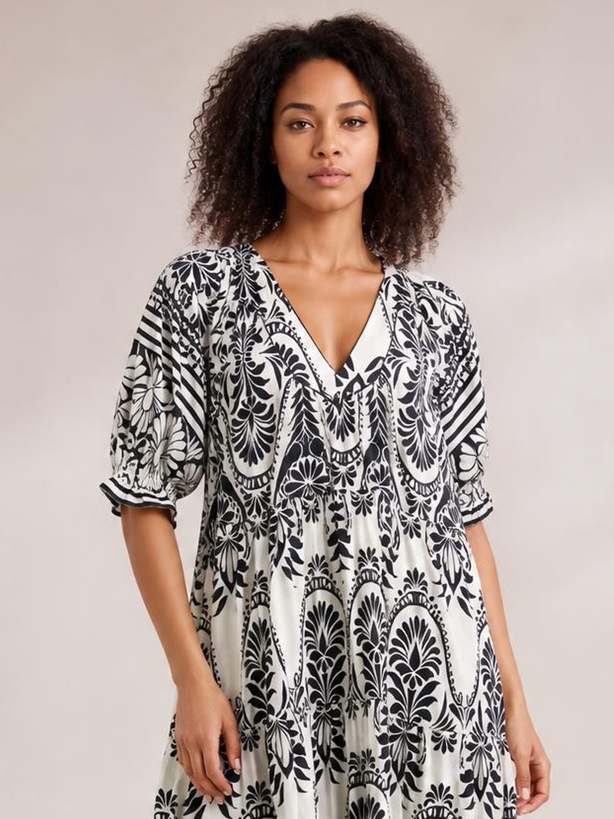 Model wears a black-and-white two-tone border print midi dress with a V-neck, three-quarter sleeves, and a relaxed, flowy tiered silhouette.