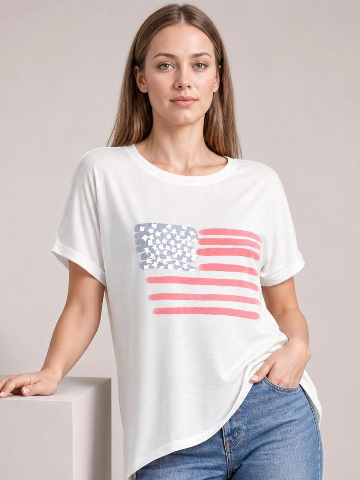 Model wearing a white US flag round neck short sleeve T-shirt with a relaxed silhouette, rolled cuffs, and red-and-blue flag graphic.