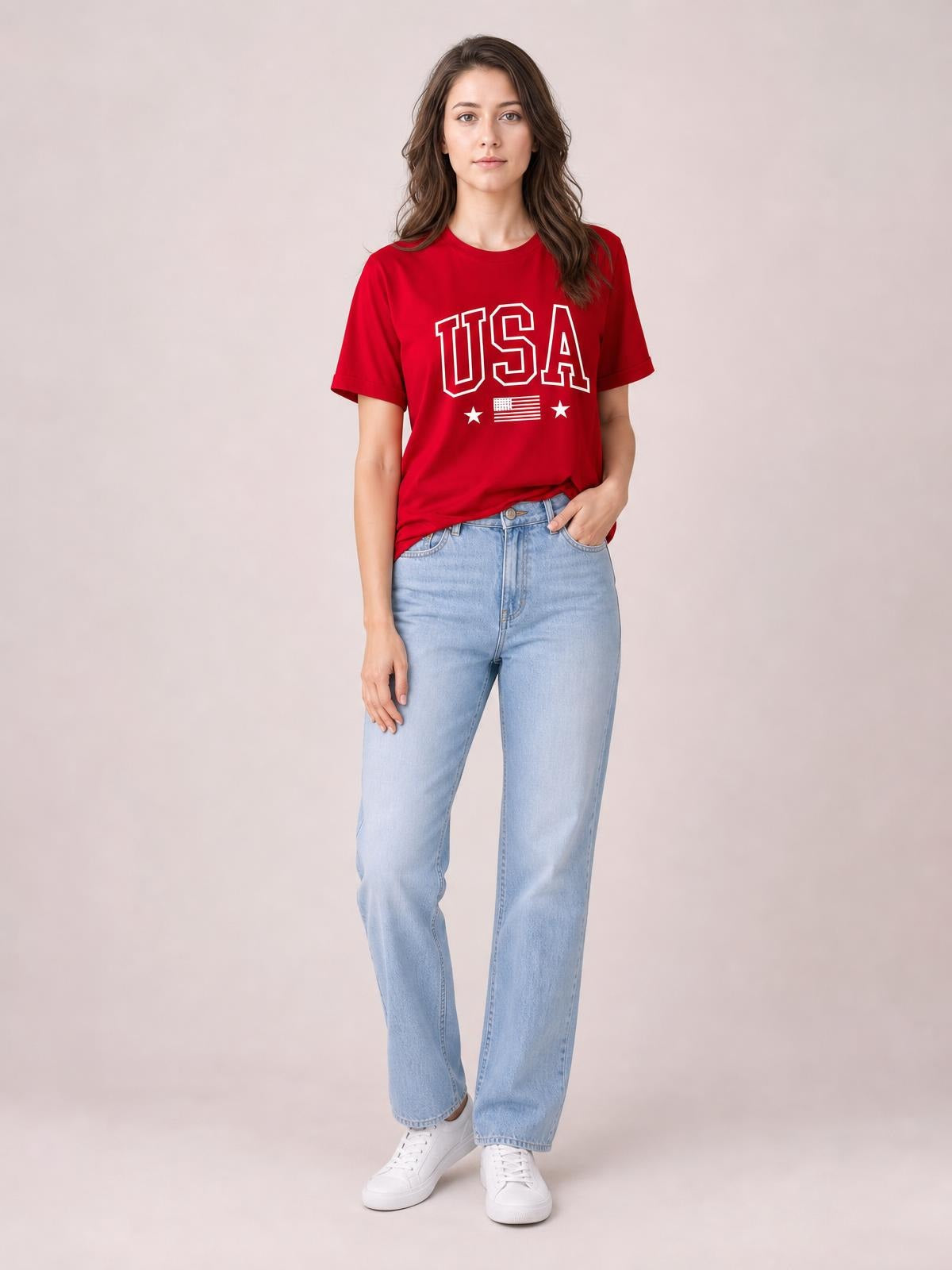 Model wearing a red USA American Flag crewneck T-shirt with short sleeves and a relaxed silhouette, posing with one hand in her jeans pocket.