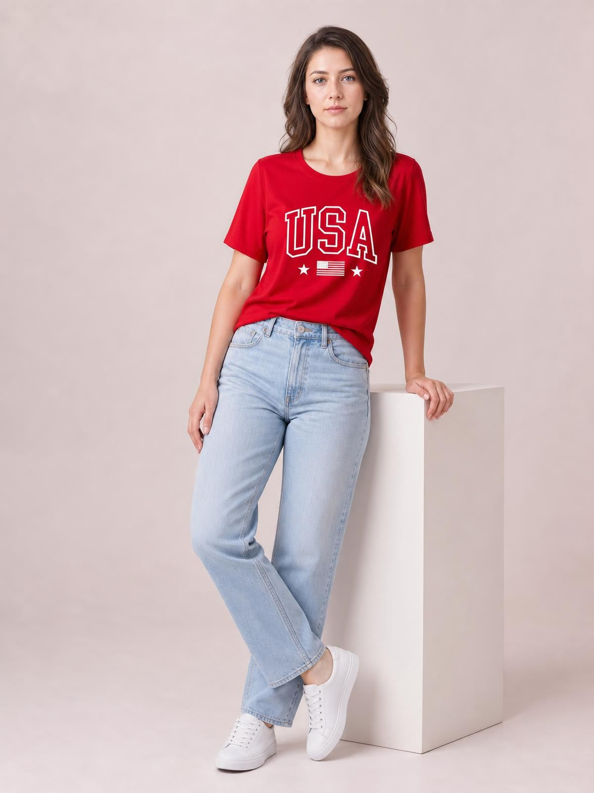 Model wears a red USA American Flag crewneck T-shirt with short sleeves, a relaxed straight silhouette, and bold white lettering, stars, and flag graphic.